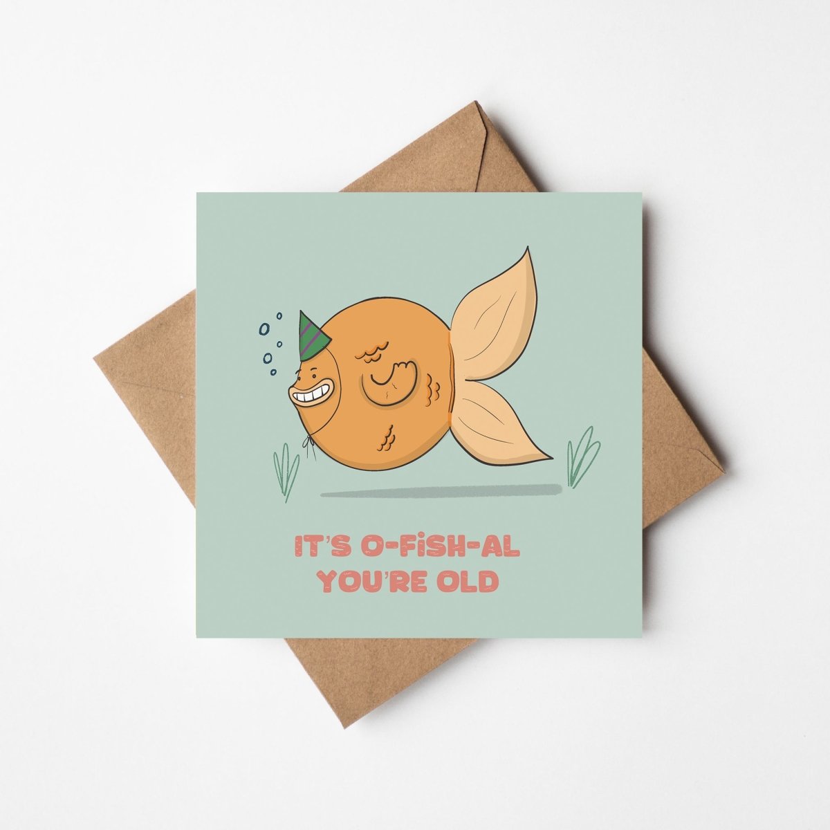 Greeting card with a fish illustration and text 'It's O-Fish-Al You're Old' on a light green background with a brown envelope.