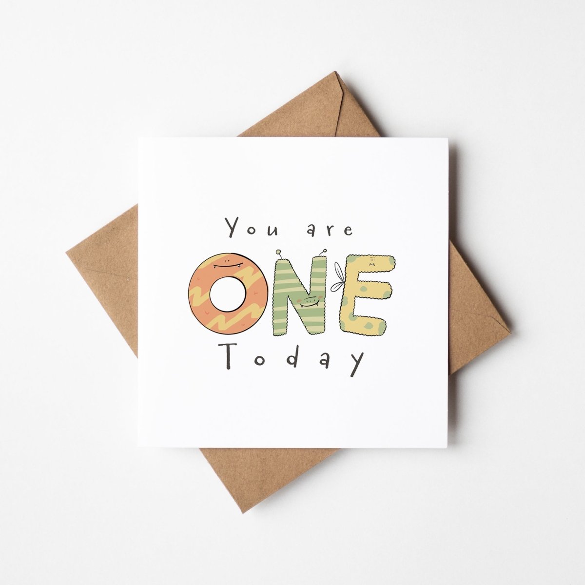 First birthday monster card mockup showing cute illustrated ONE letters with kraft envelope