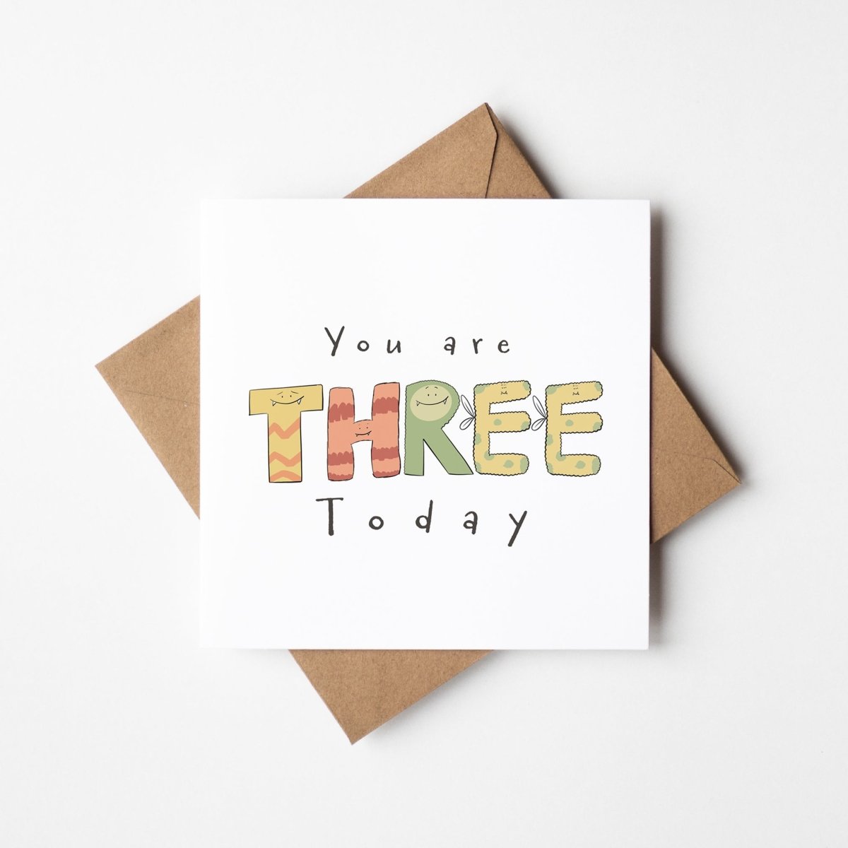 Third birthday monster card mockup showing cute illustrated THREE letters with kraft envelope